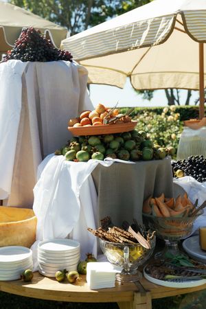 A buffet table set outdoors with white linens displaying various dishes, fruits, and appetizers in elegant serving bowls.