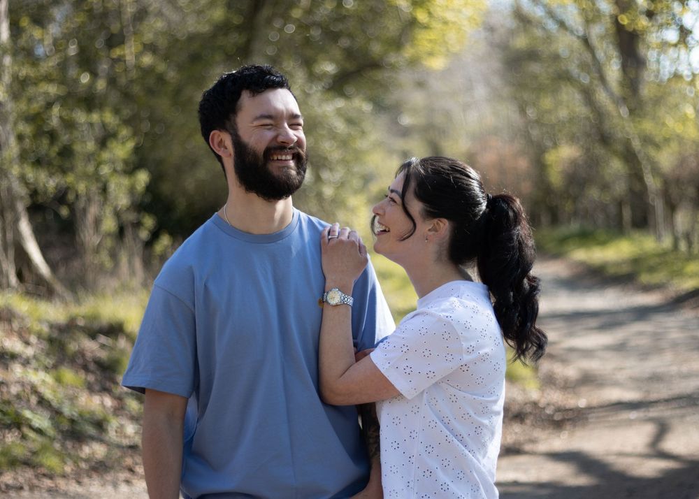 A couple shares tender moments while walking together on a tree-lined path during a sunny autumn day.