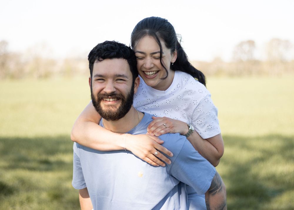 A couple embraces lovingly in a sunlit meadow while wearing casual blue and white clothing.