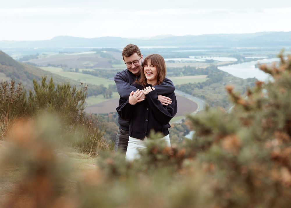 A couple embraces while enjoying scenic mountain views on a sunny afternoon in nature.