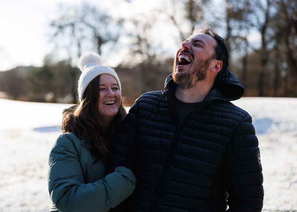 A couple shares a joyful laugh together while enjoying a snowy winter day outdoors.