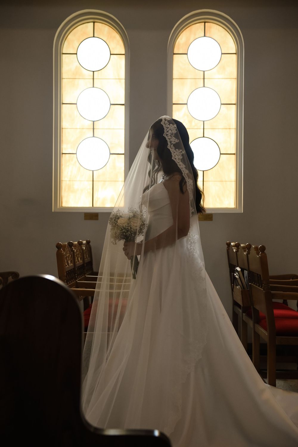 Sunlight streams through arched church windows, illuminating a wedding dress silhouette in a chapel.