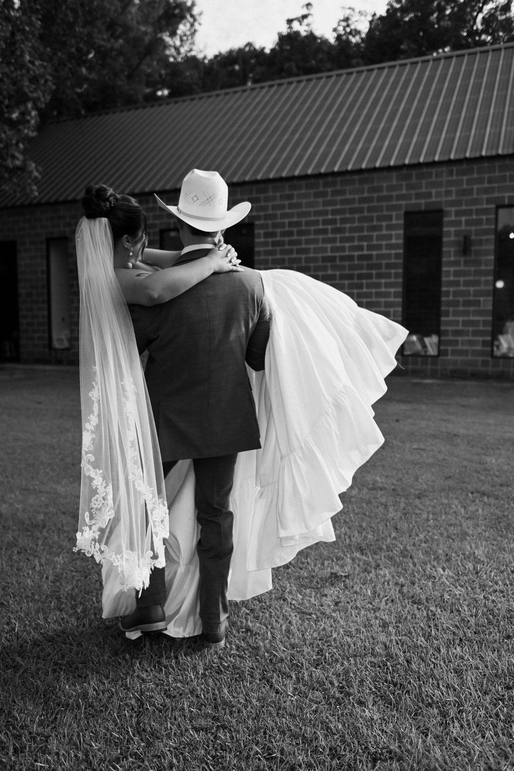 A black and white photo of a couple walking on grass, with the bride's white dress flowing in the wind.
