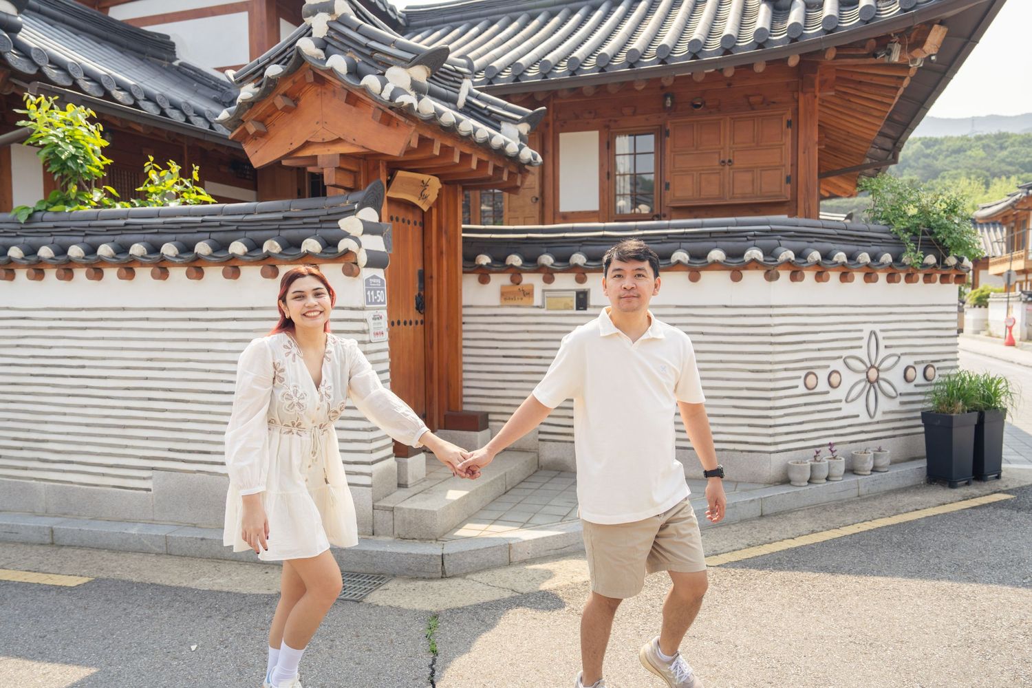 People walking past traditional Korean hanok buildings with curved tile roofs and wooden architecture on a sunny day.
