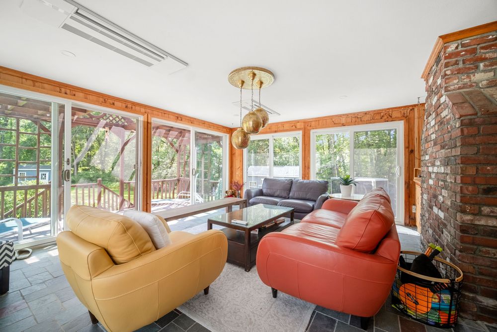 Sunlit living room with wood-paneled walls, leather sofas, pendant lighting, and views of lush greenery outside.