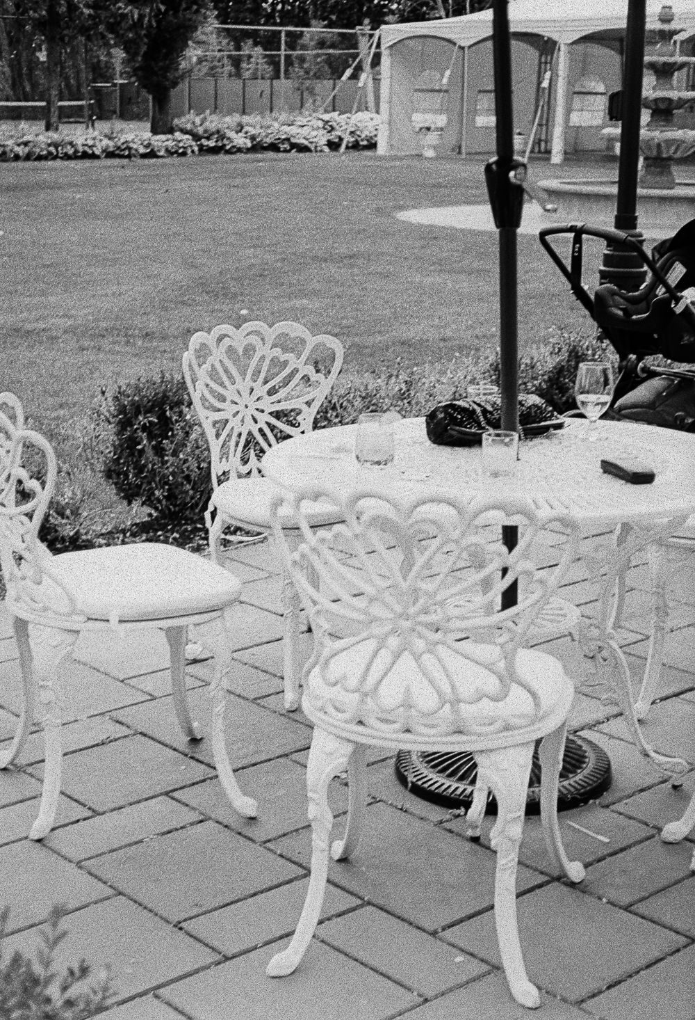 White ornate garden chairs and tables arranged on a stone patio create an elegant outdoor seating area.