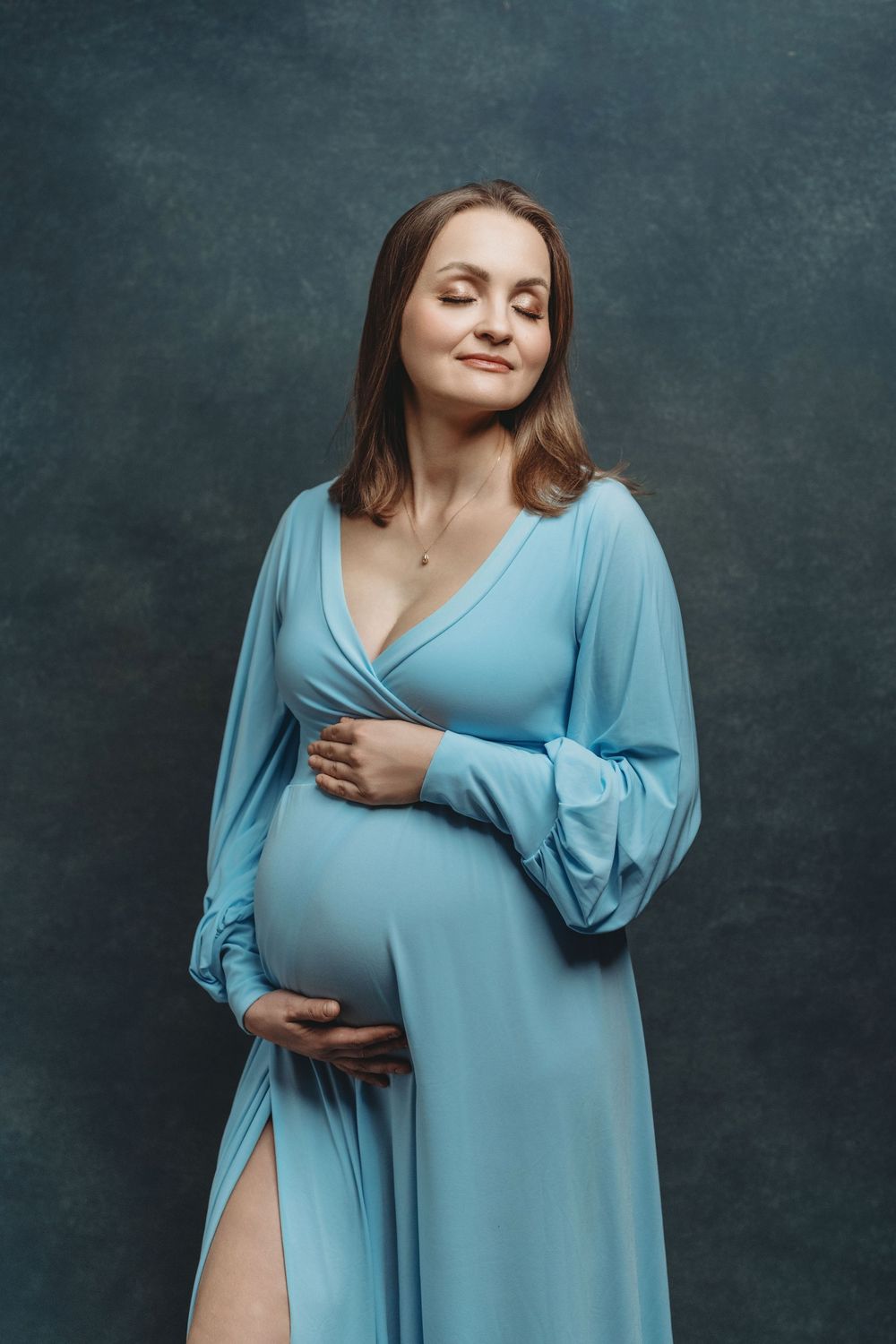 A woman in a flowing light blue dress poses expressively against a dark textured background.