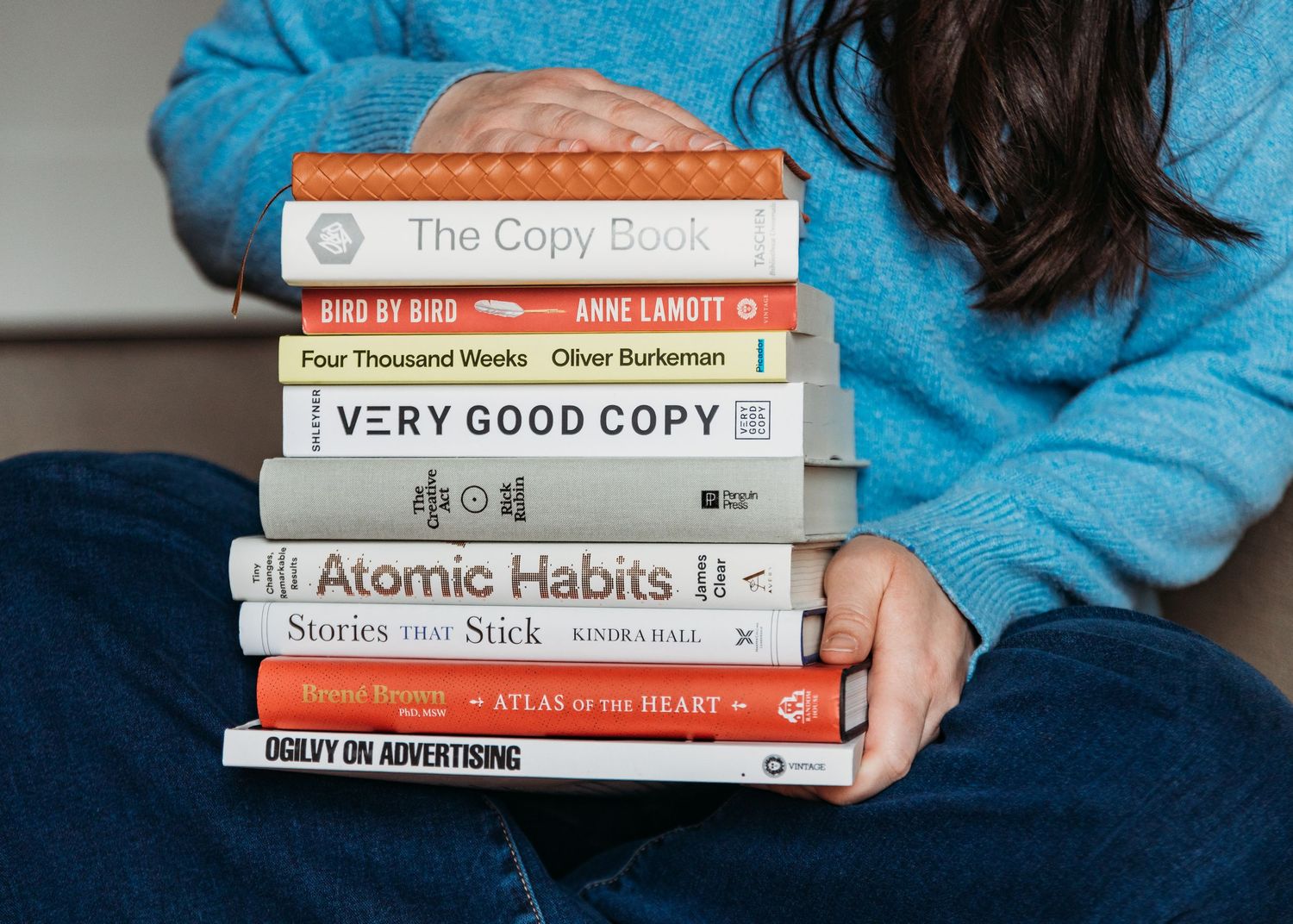 Stack of self-help and personal development books held by someone wearing a blue sweater.