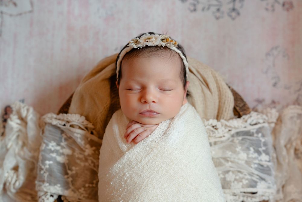 A sleeping newborn wrapped in delicate white lace swaddle against a soft neutral background.