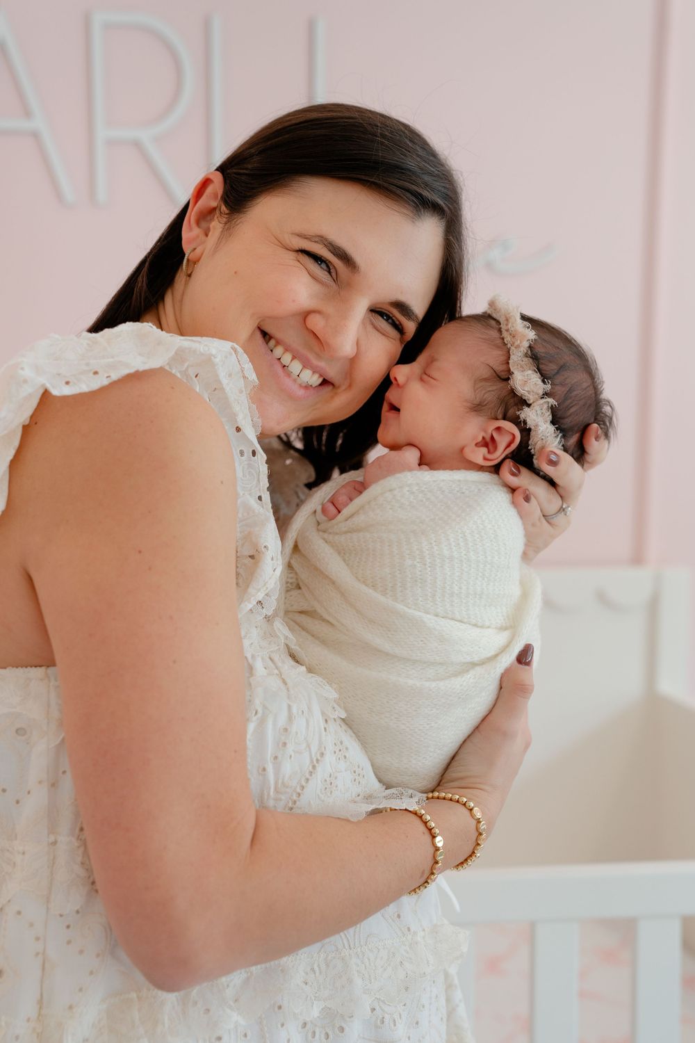 A tender moment between parent and baby in soft pink lighting with white clothing.