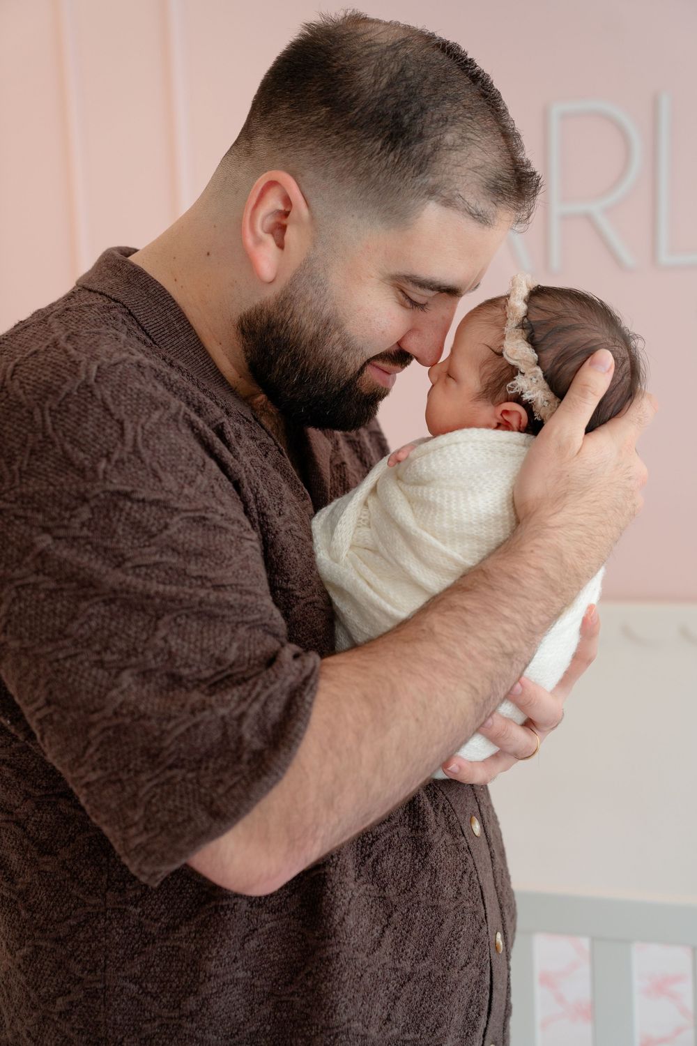 Tender moment captured in nursery room with soft pink walls.