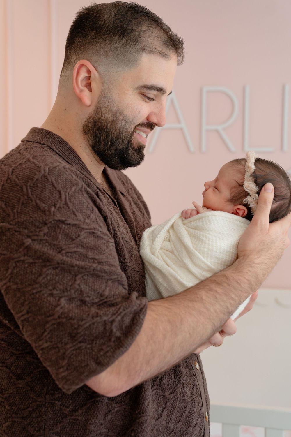 Gentle embrace shared in nursery with pink wall backdrop.