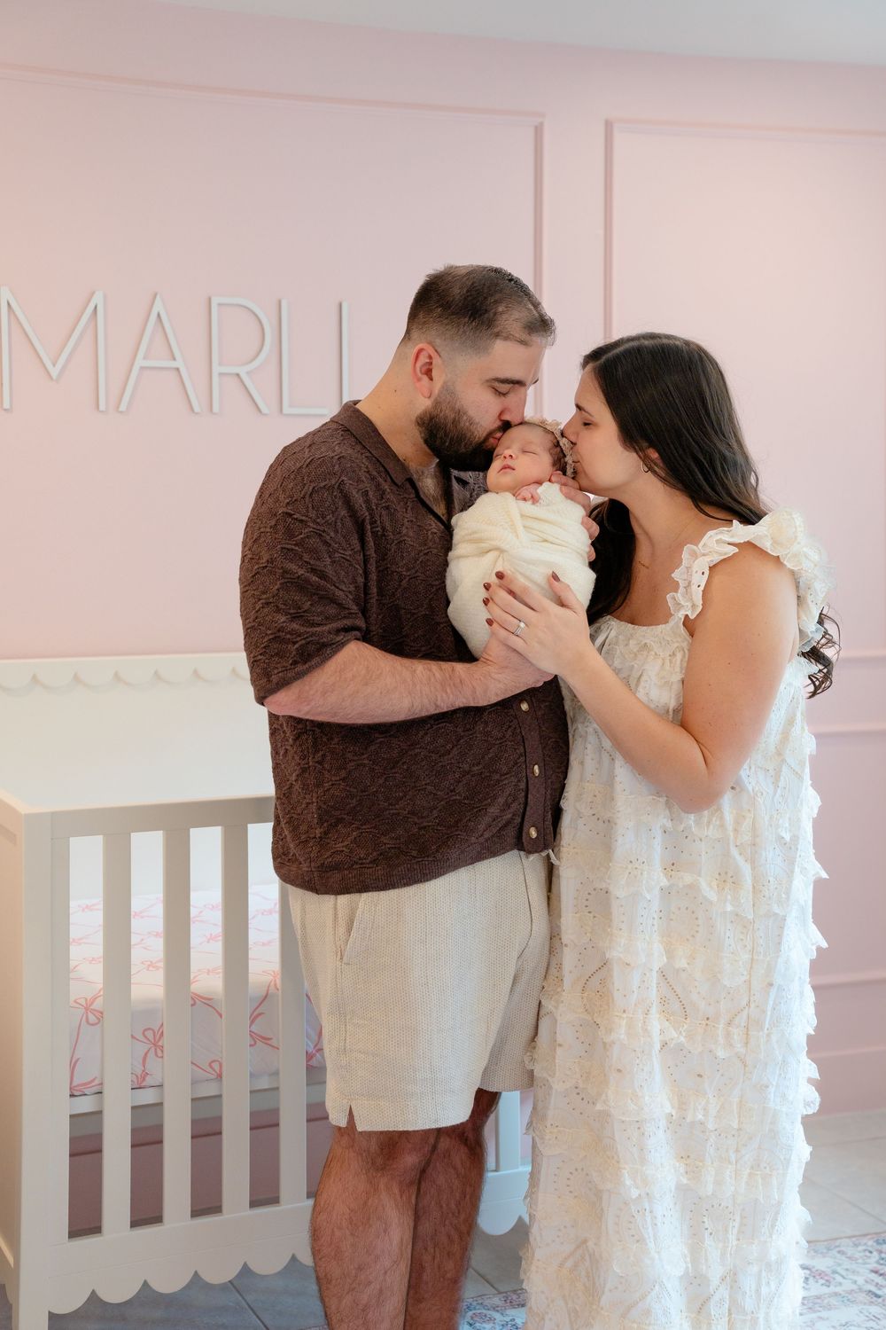 Sweet family moment captured in nursery with white crib and pink walls.