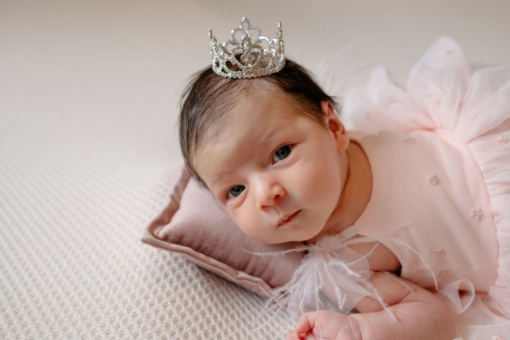 Newborn baby wearing a delicate crown and pink tulle dress lying on soft white bedding in a series of portraits.