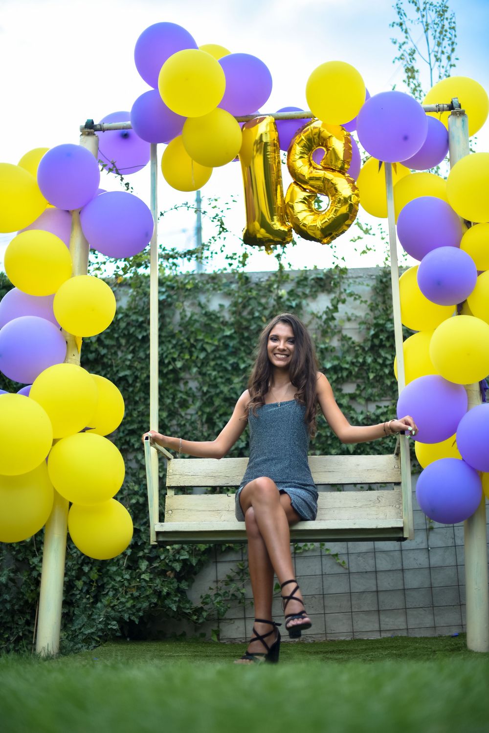 Purple and yellow balloons decorate an outdoor garden fence creating a festive party backdrop.