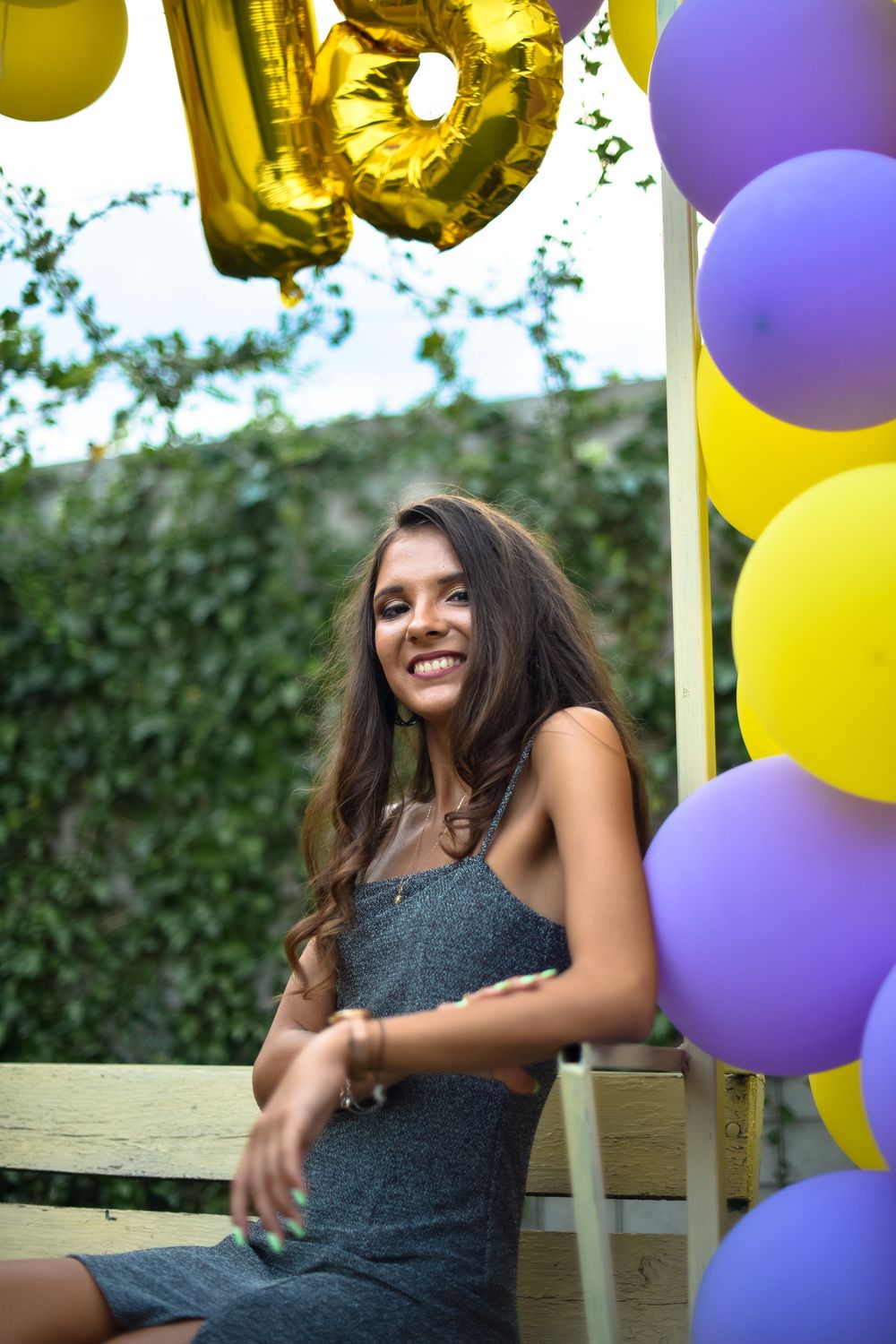 A festive outdoor photoshoot setup with purple and yellow balloons against an ivy-covered wall.