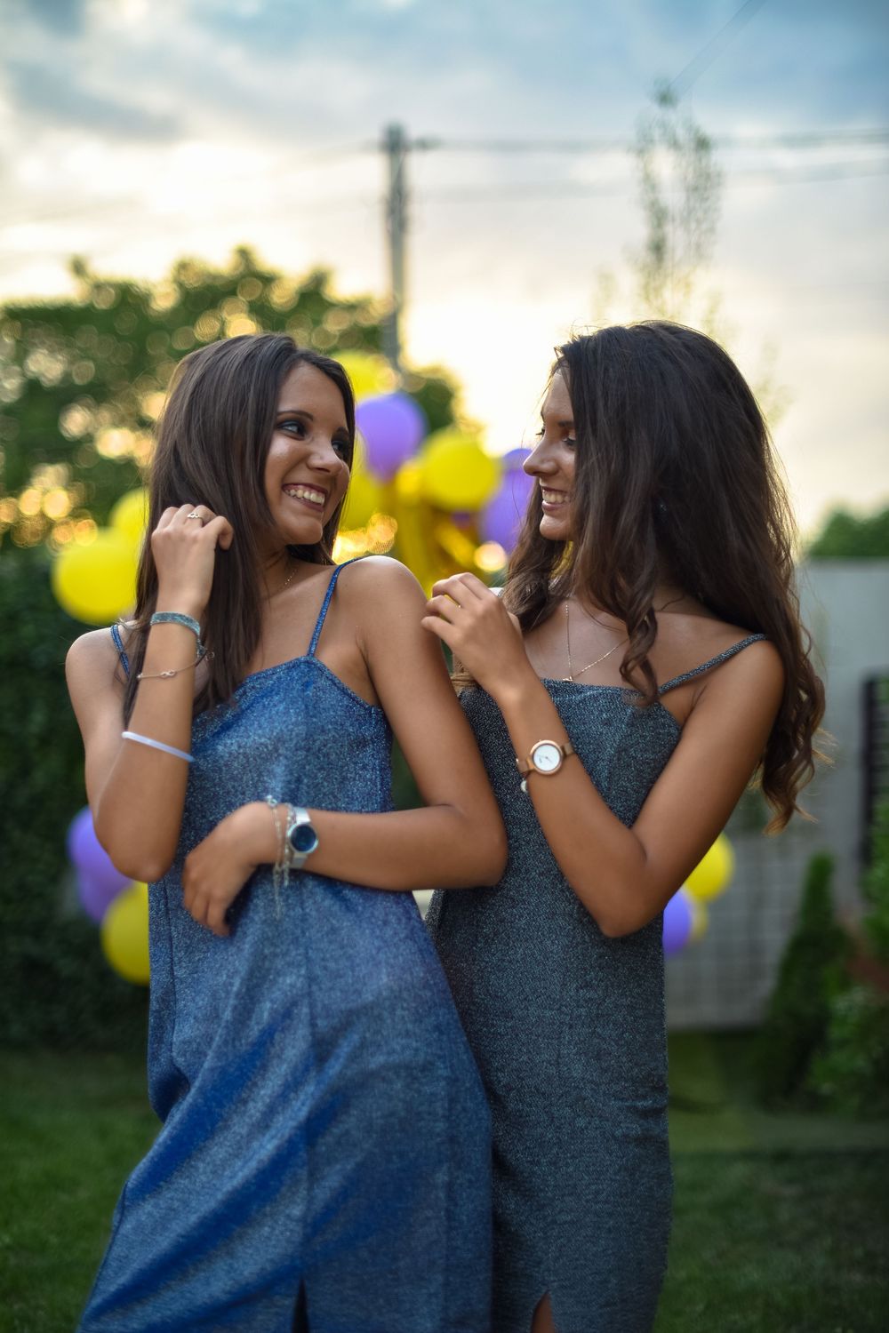 Two friends in blue sleeveless tops share joyful laughter together outdoors at sunset.
