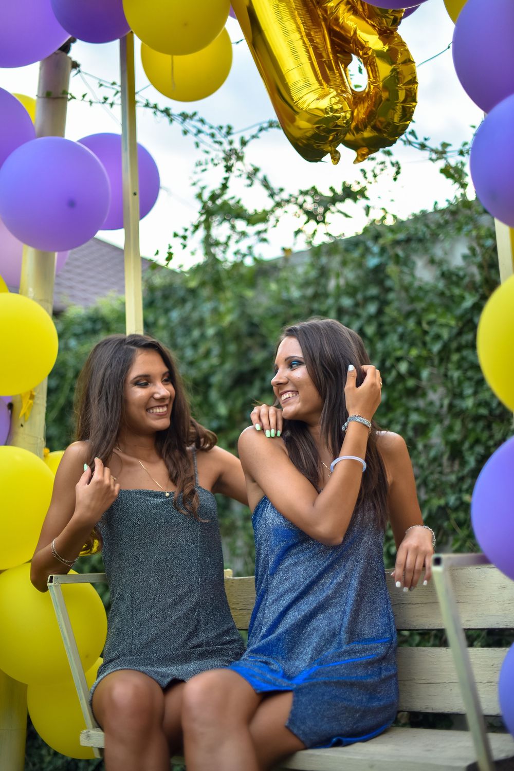 Friends laughing together outdoors surrounded by purple and yellow balloons at a celebration party.