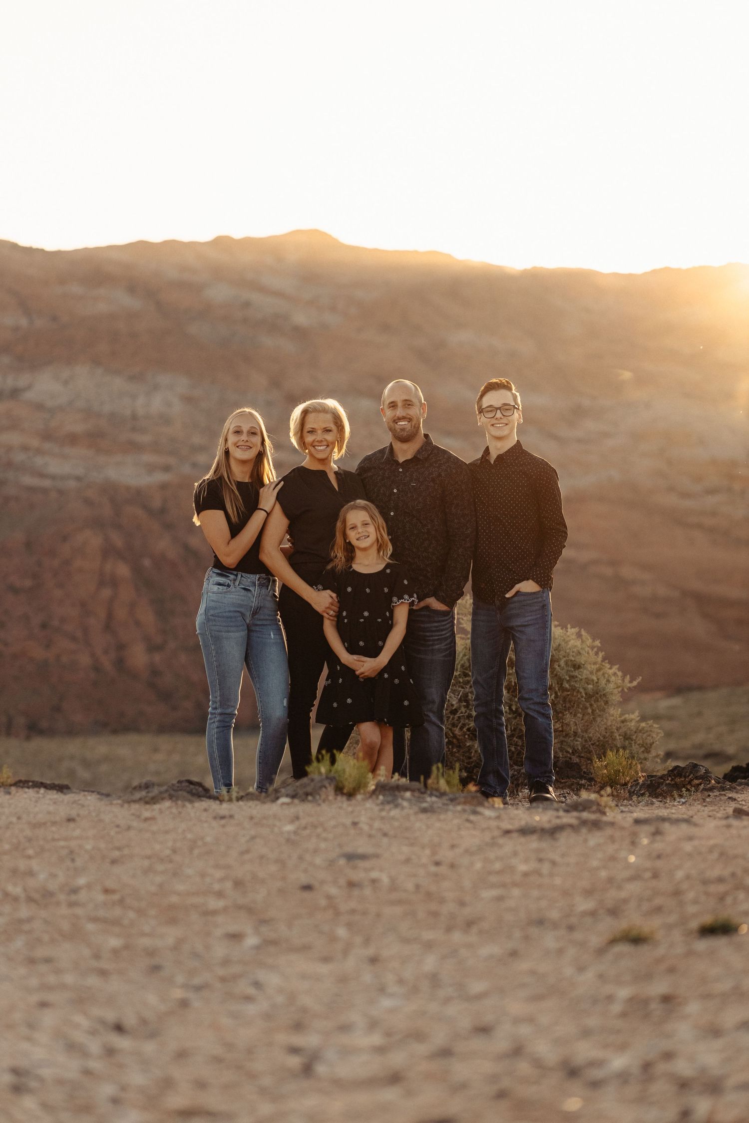 Family group poses together against scenic desert canyon backdrop during golden hour sunset.