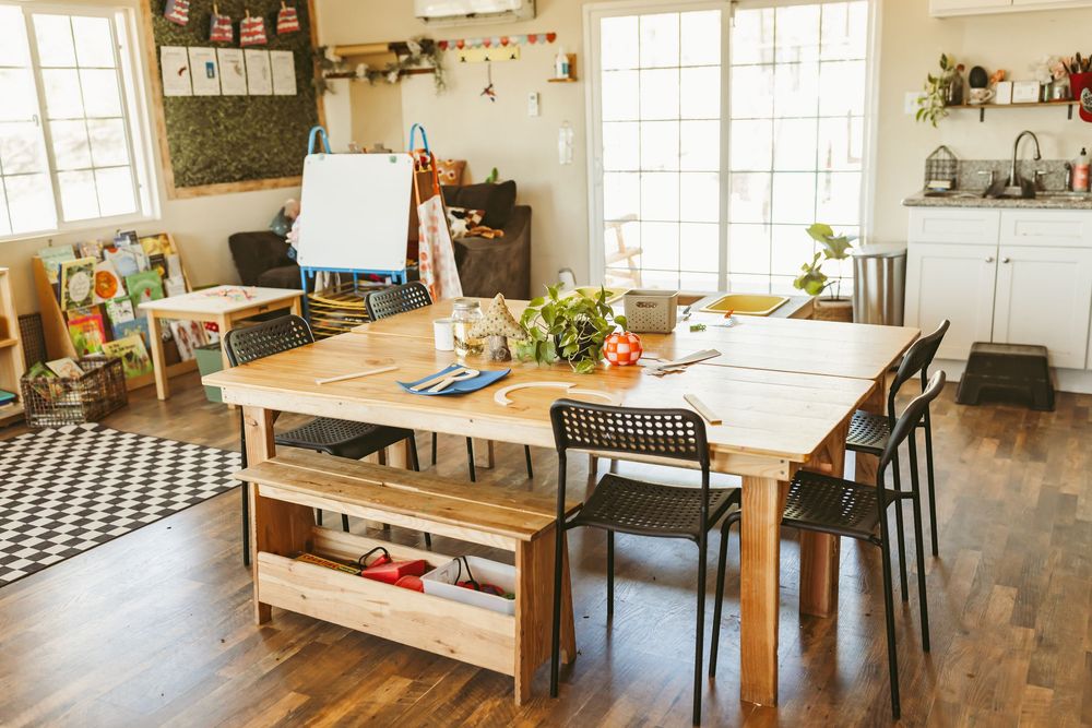A bright, modern dining room with hardwood floors features a rustic wooden table, bench seating and black chairs.