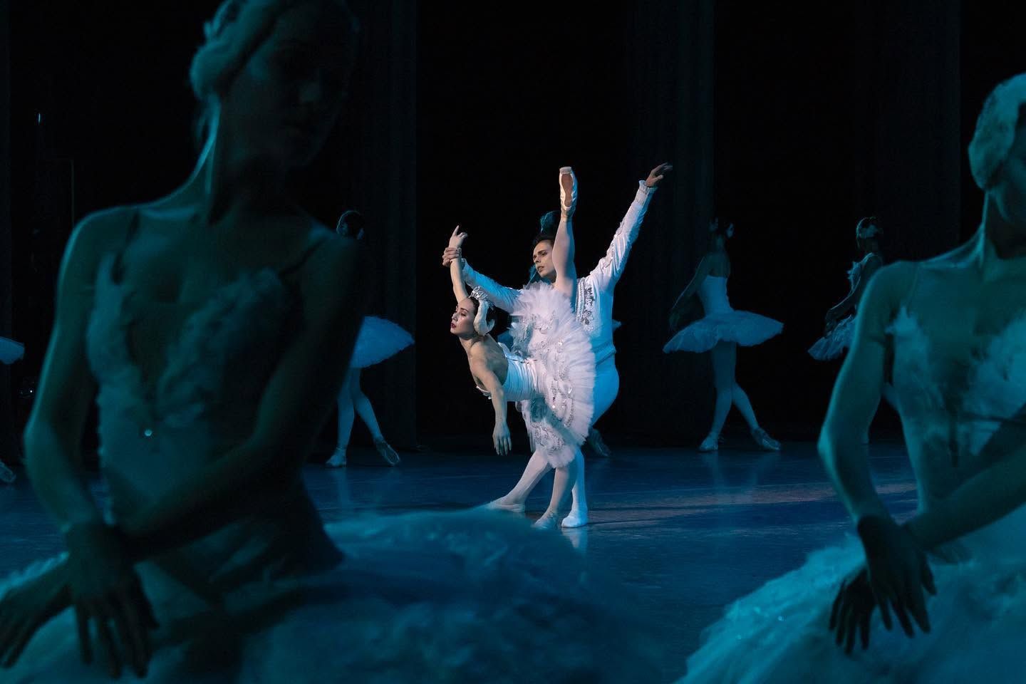 Ballet dancers performing Swan Lake on dark stage with corps de ballet in white tutus.
