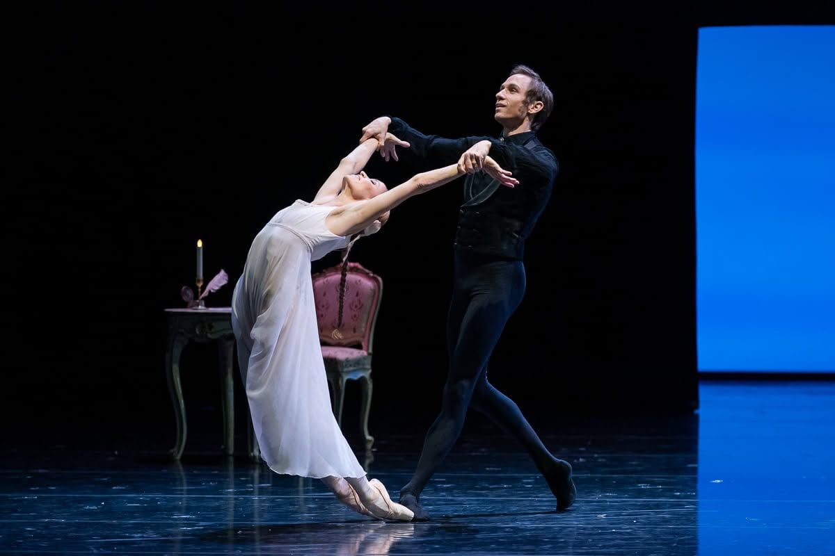 Ballet couple performing a graceful romantic pas de deux on a theatrical stage with props.