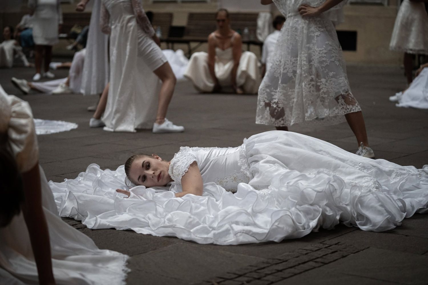 A woman in a large white wedding dress lies on the ground surrounded by other performers.