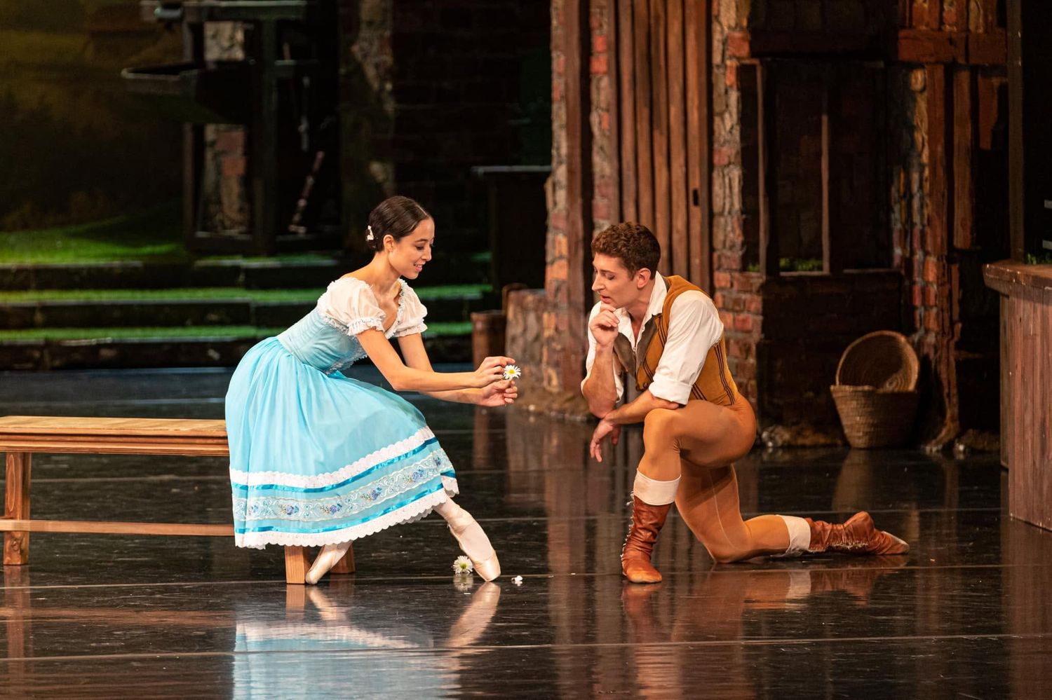 Two ballet dancers perform a romantic pas de deux in a rustic village stage set during a classical ballet.