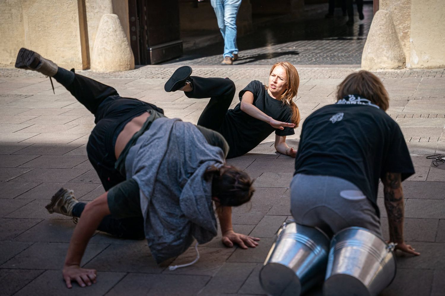 Three performers doing contemporary street dance on an urban pavement, one doing a handstand.