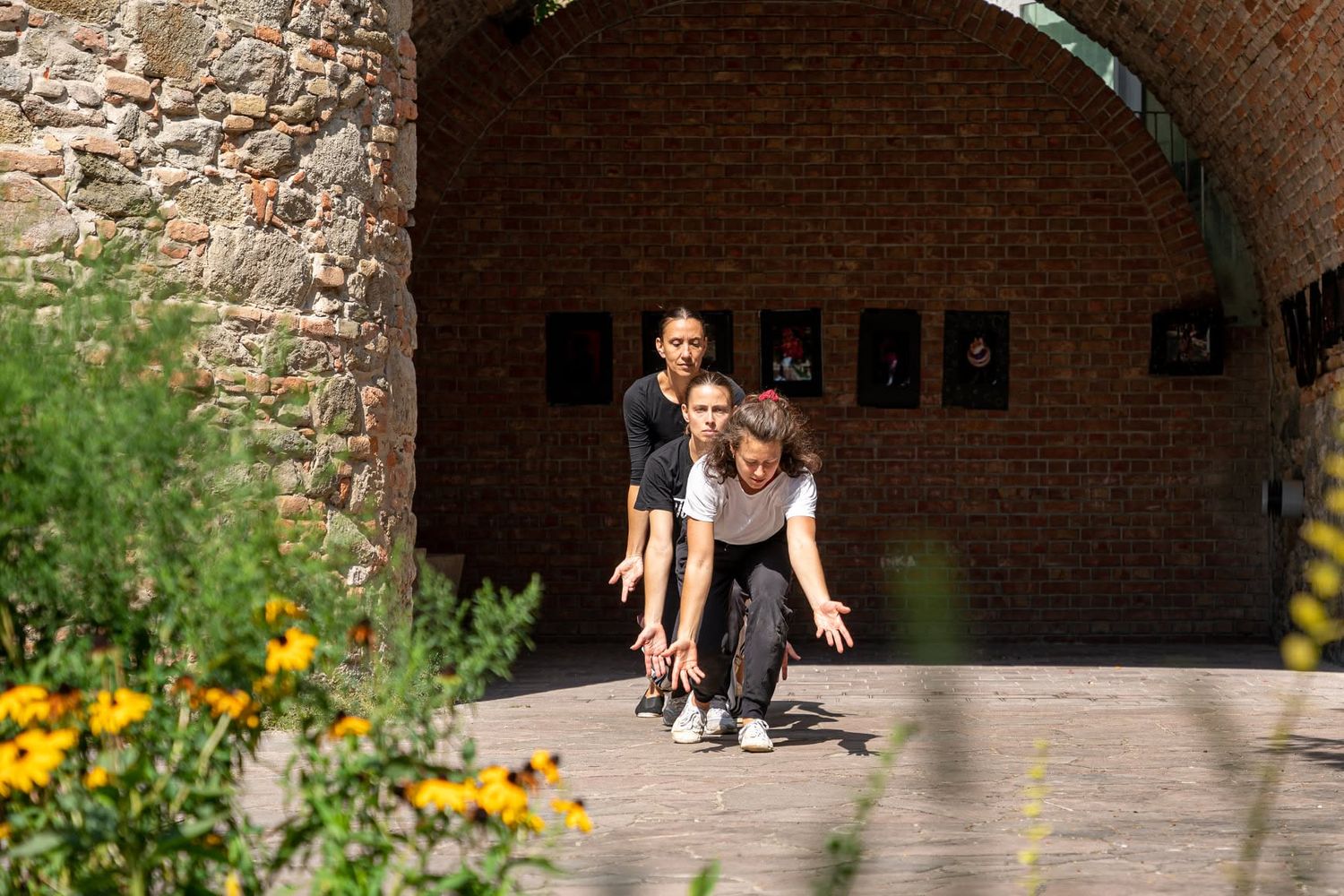 Two dancers performing contemporary dance under a brick archway with yellow flowers in foreground.