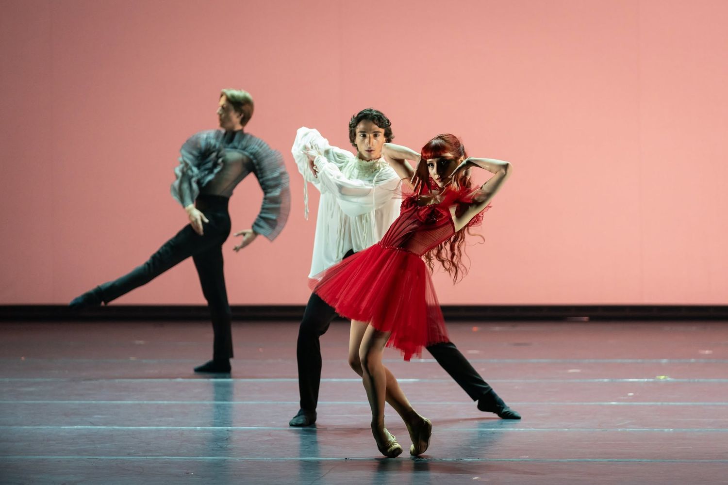 Three contemporary ballet dancers perform an expressive modern dance piece on a pink-lit stage.