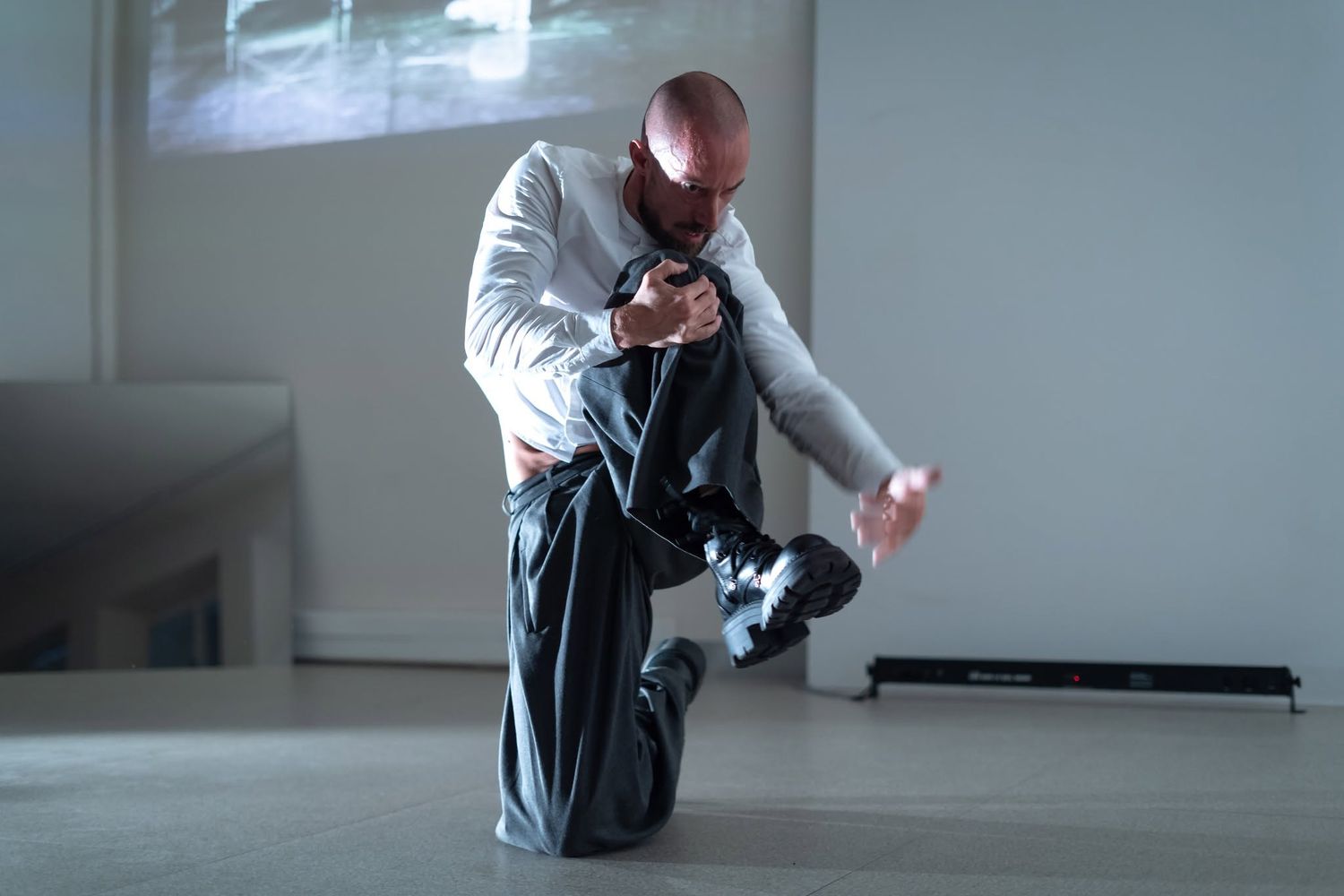 Male dancer in white shirt performs an expressive solo contemporary dance piece in a gallery space.