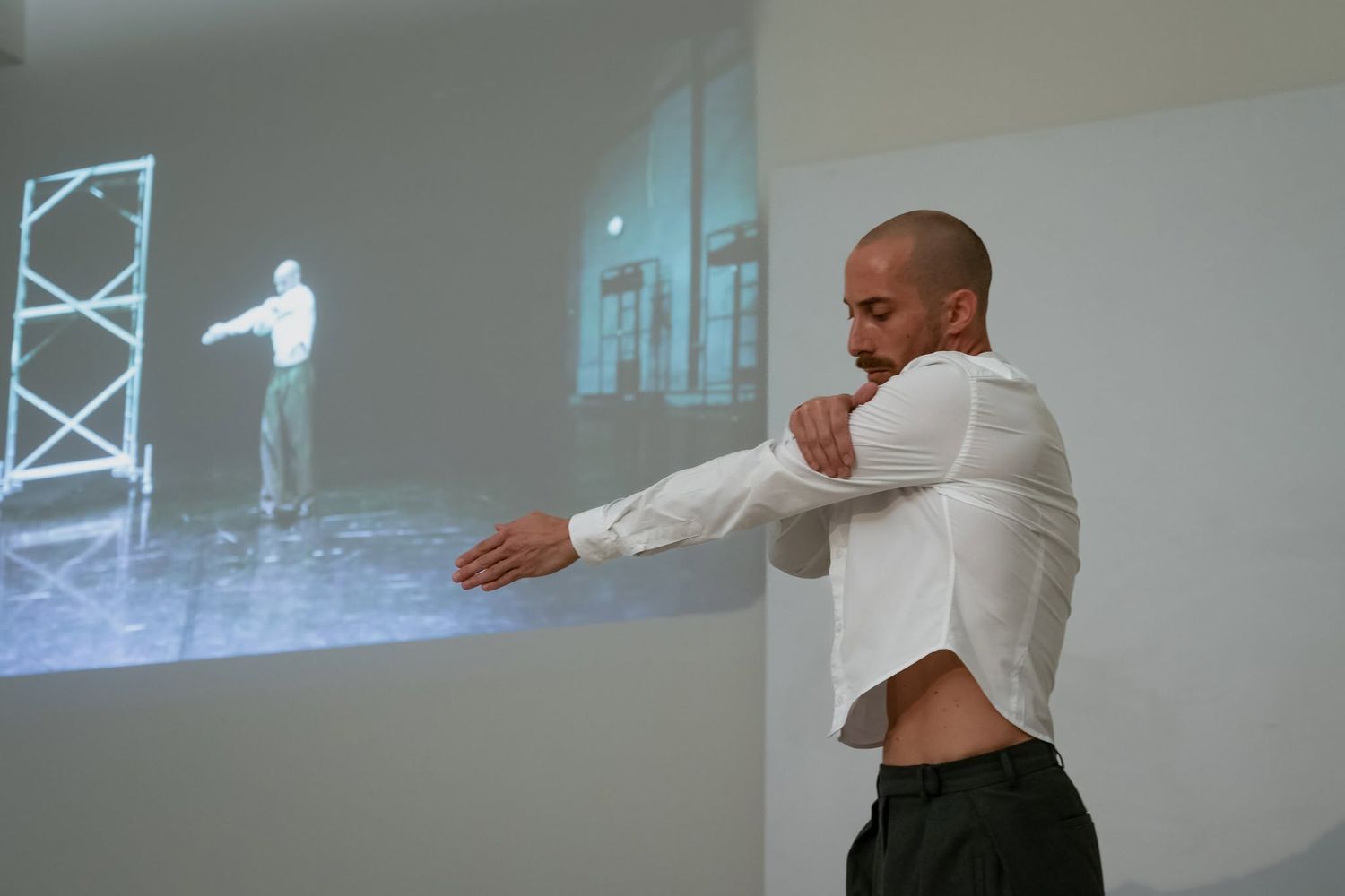 Male dancer in white shirt mirrors projected video performance in a contemporary dance art installation.