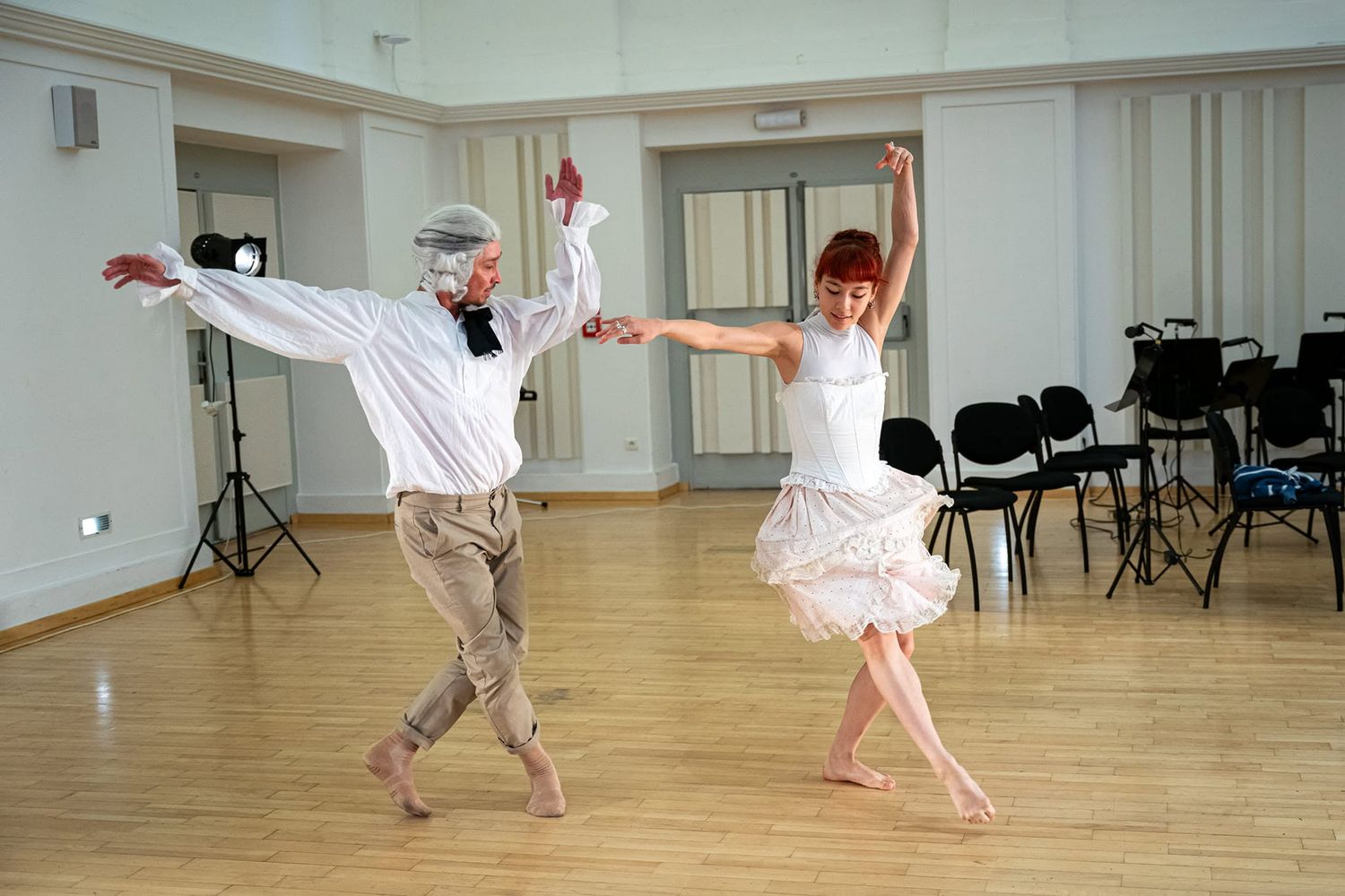 Two dancers rehearse in a bright studio, performing an elegant ballroom routine in period costumes.