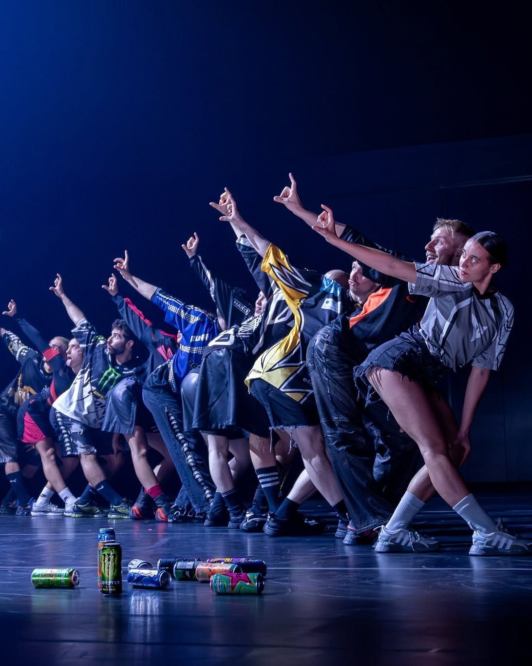 Large group of dancers in colorful sportswear perform an energetic routine on stage with energy drink cans.