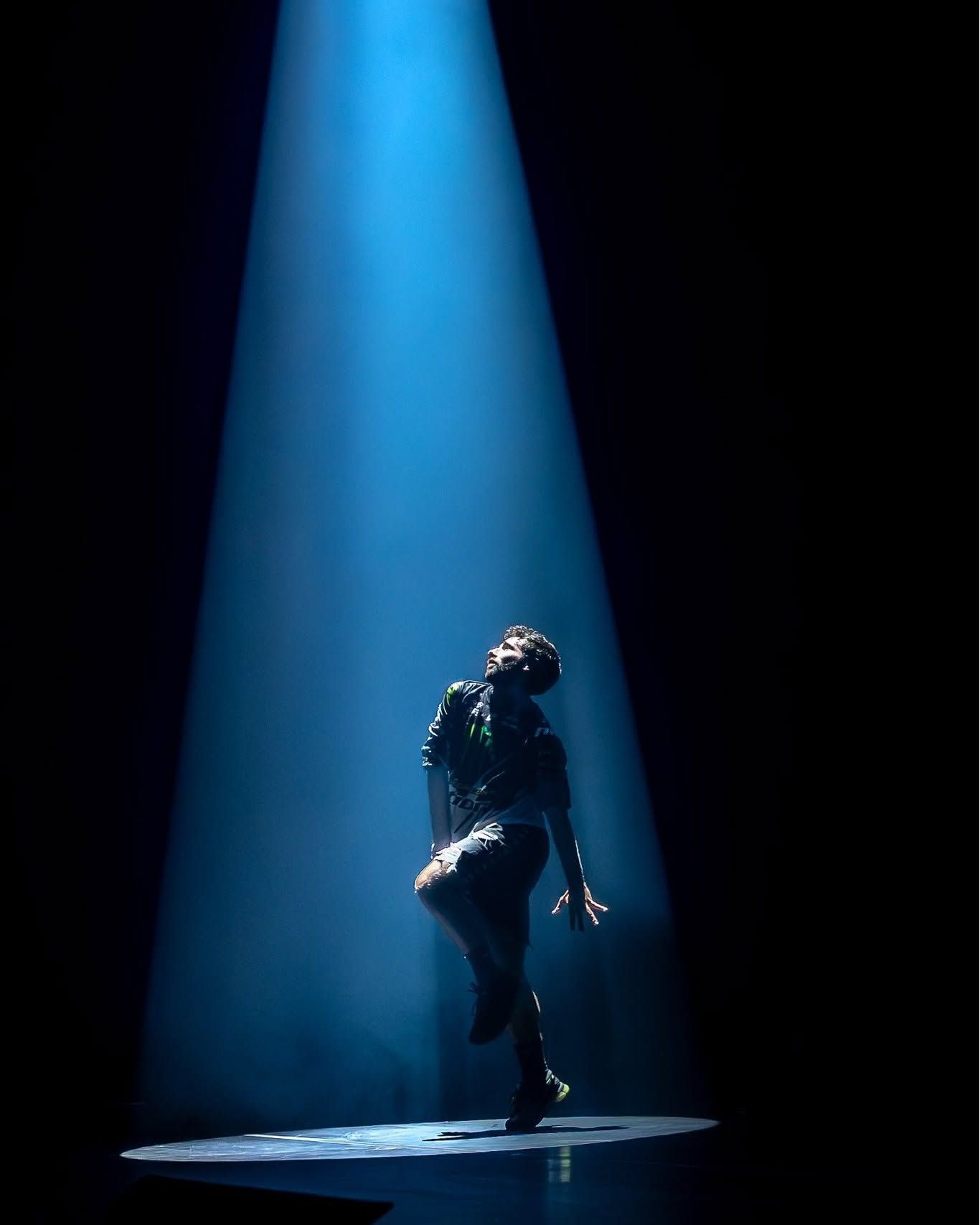 Solo dancer performs under a dramatic blue spotlight on a dark stage in a captivating dance performance.