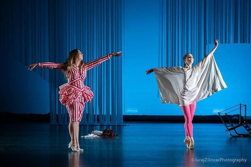 Two ballet dancers perform on a blue-lit stage in colorful costumes during a theatrical production.