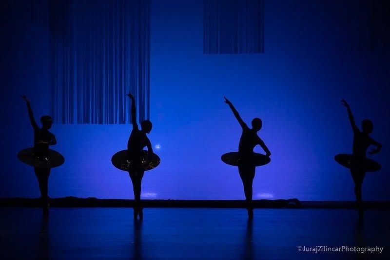 Four ballet dancers silhouetted in arabesque pose against a vivid blue-lit stage background.