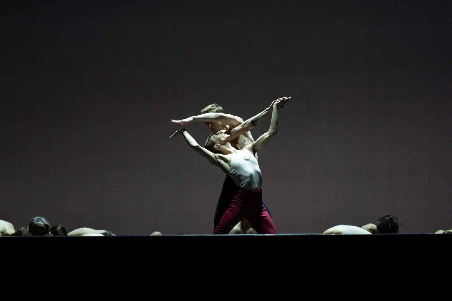 Two contemporary dancers perform an expressive duet under dramatic spotlight on a minimalist dark stage.