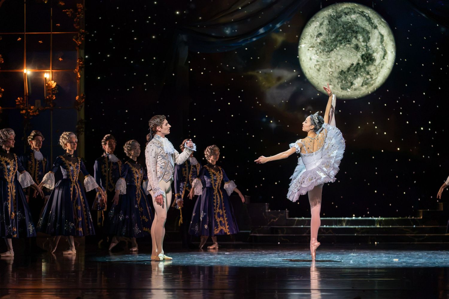 Two ballet dancers perform on stage with a large moon backdrop and ensemble cast in a stunning Nutcracker production.