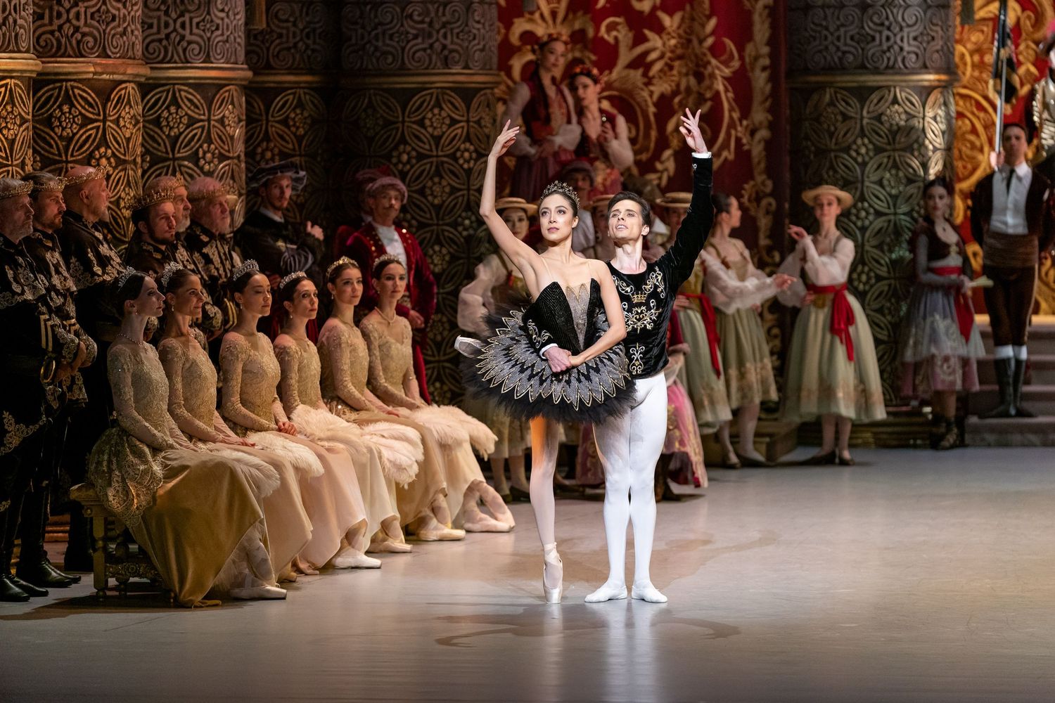 Ballerina in black tutu takes bow with partner during Swan Lake performance on stage.