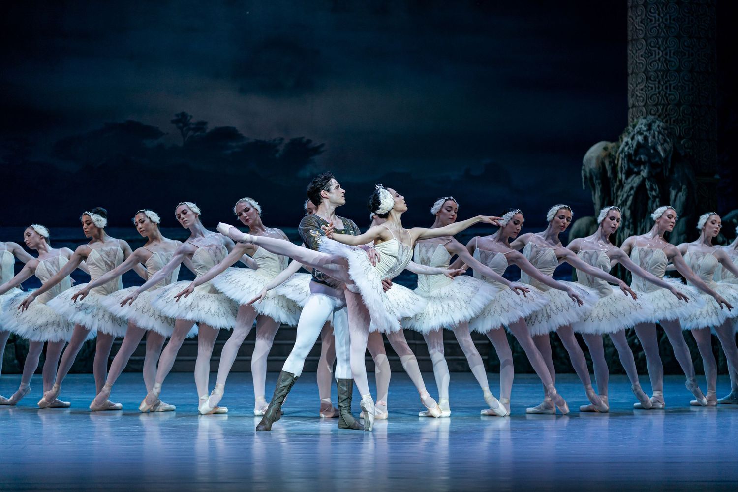 Ballet couple performs romantic pas de deux surrounded by symmetrical line of corps de ballet in white tutus.