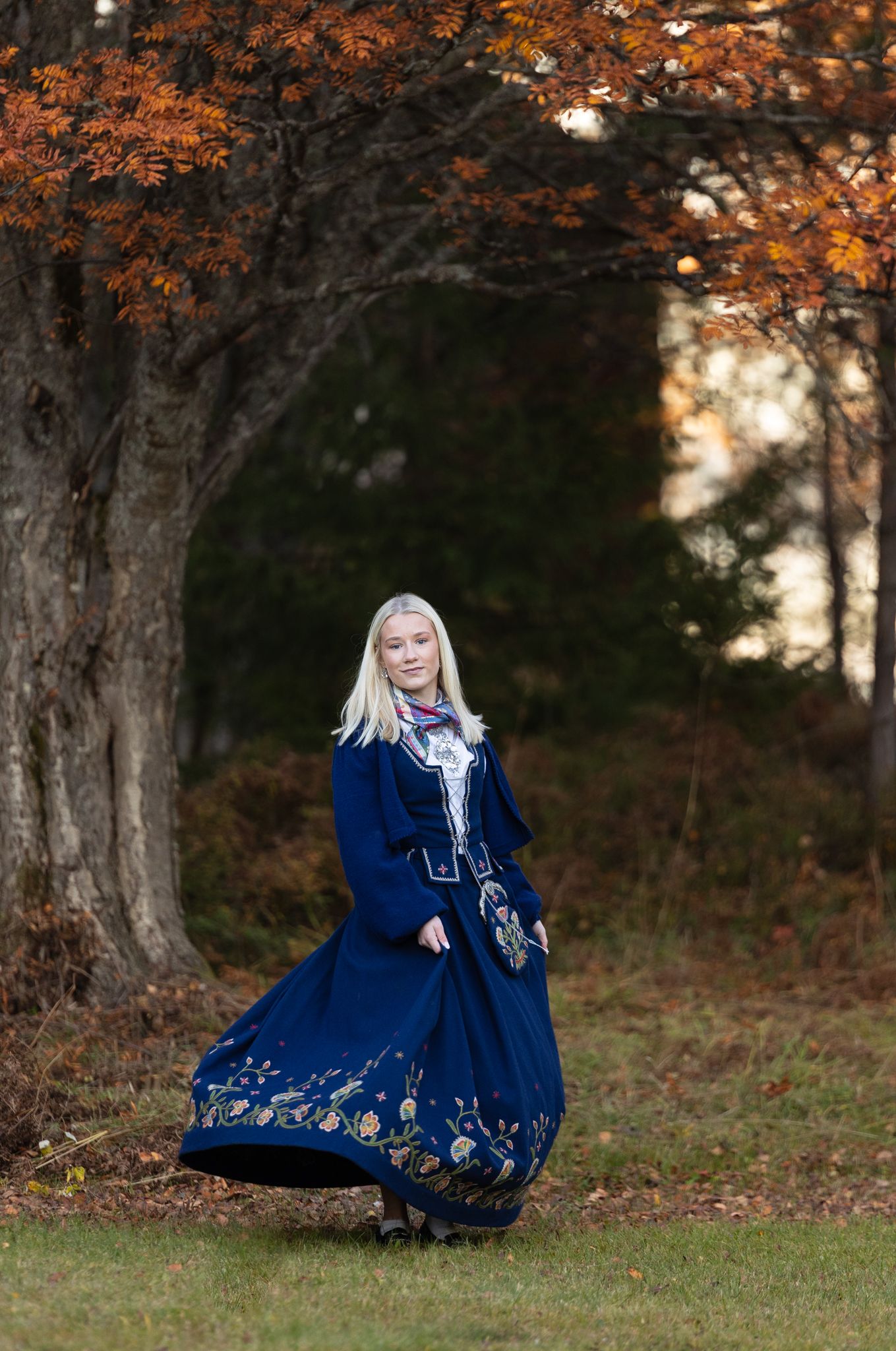 Traditional navy blue folk dress with embroidered details photographed in autumn forest setting.