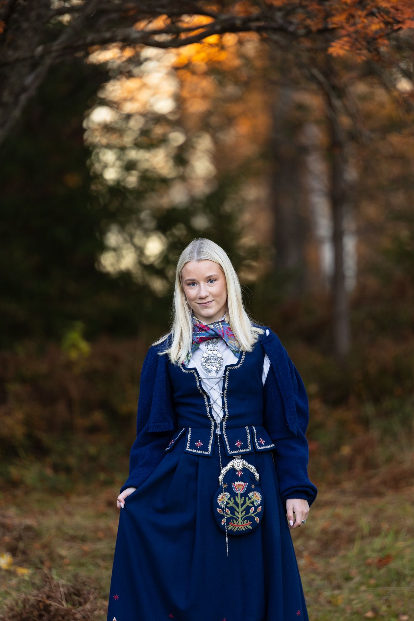 Folk dress featuring navy blue fabric with floral embroidery in autumn woodland setting.