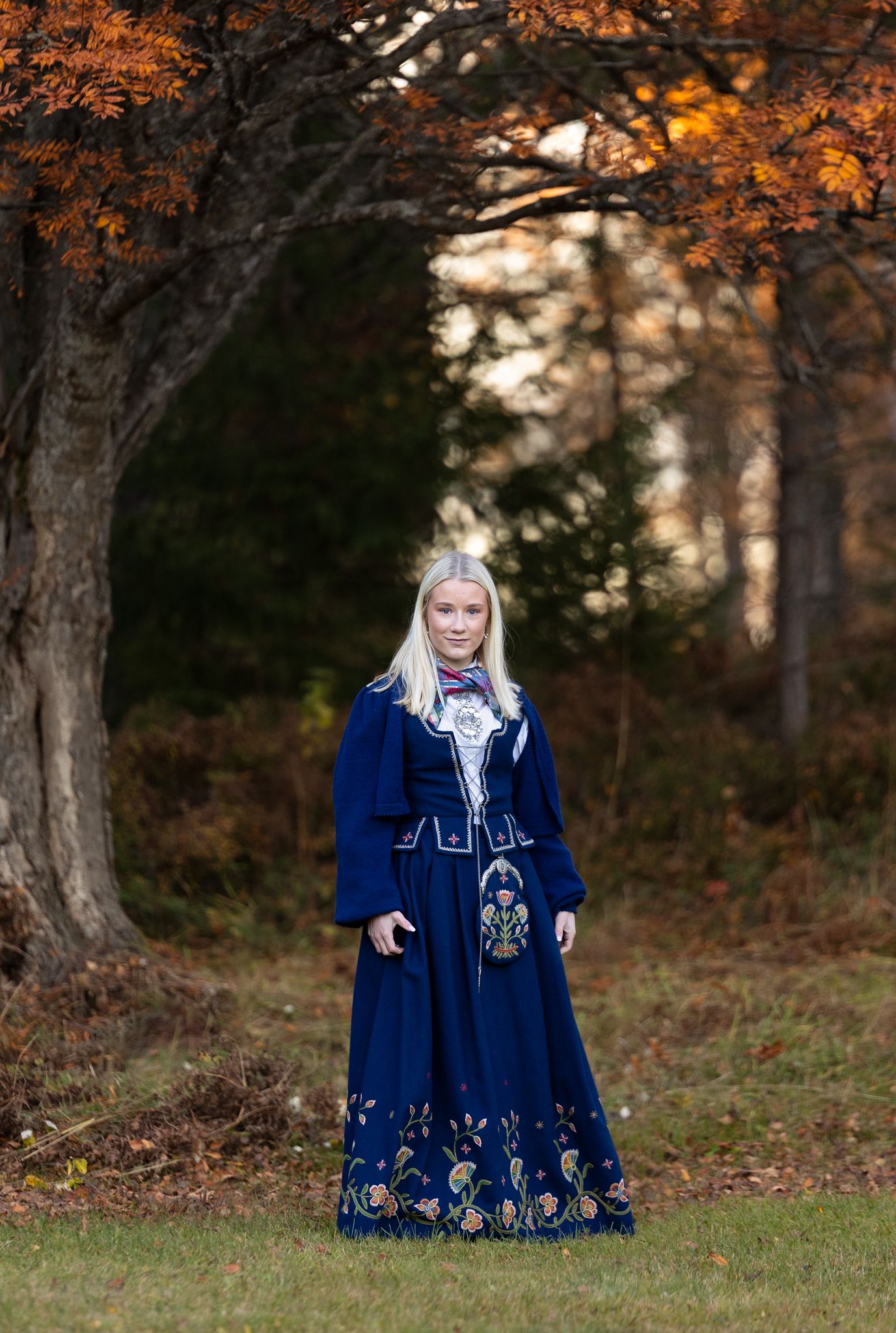 Navy blue folk dress with intricate embroidery photographed under autumn trees.