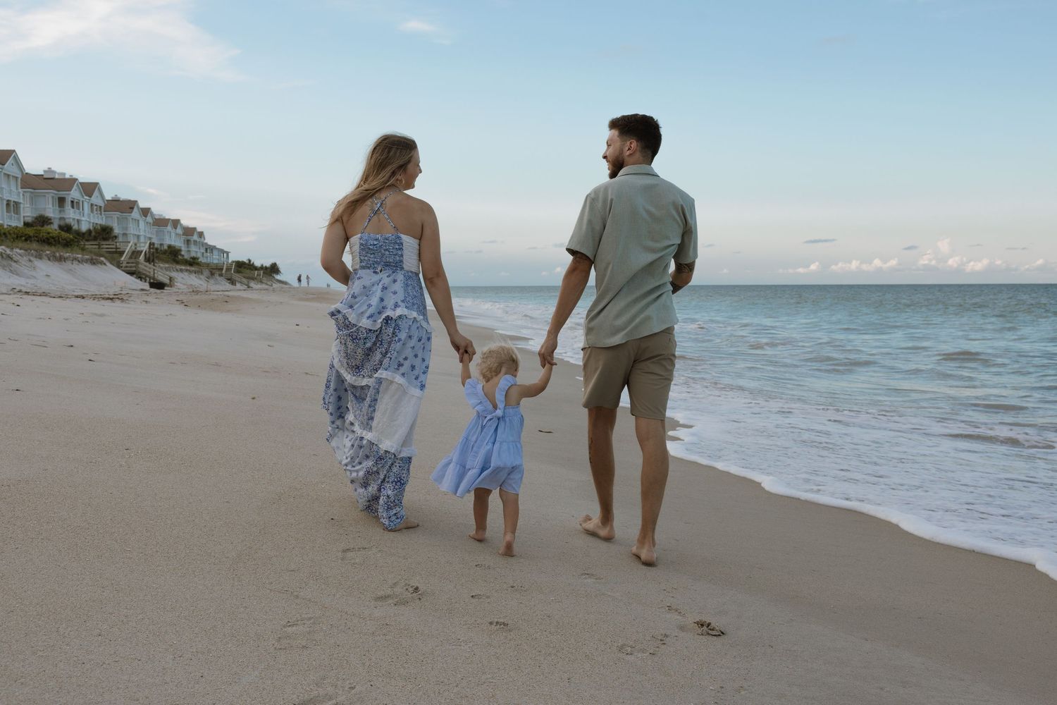 Family walks along sandy beach holding hands while enjoying a sunset stroll by the ocean.