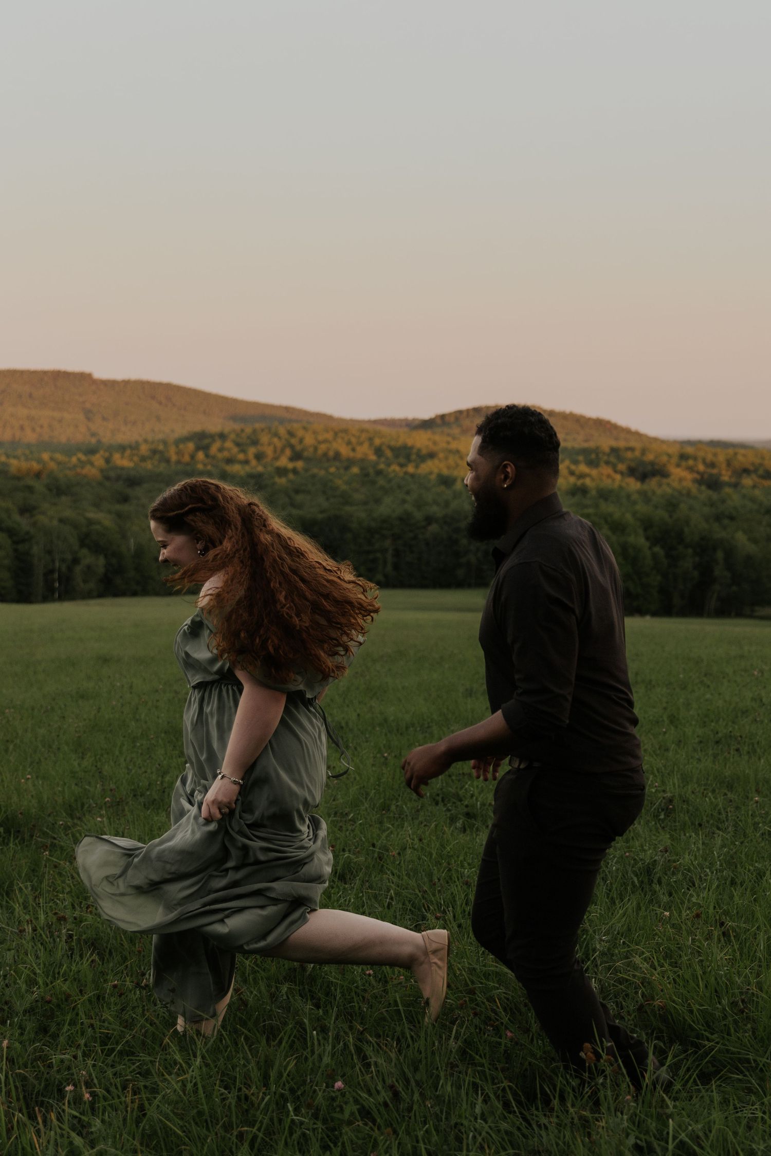 Dancing figures in a meadow with rolling hills during golden hour.
