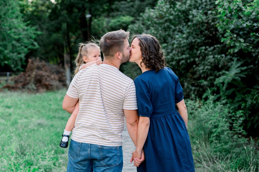 A family holding hands walks together through a lush green summer landscape.