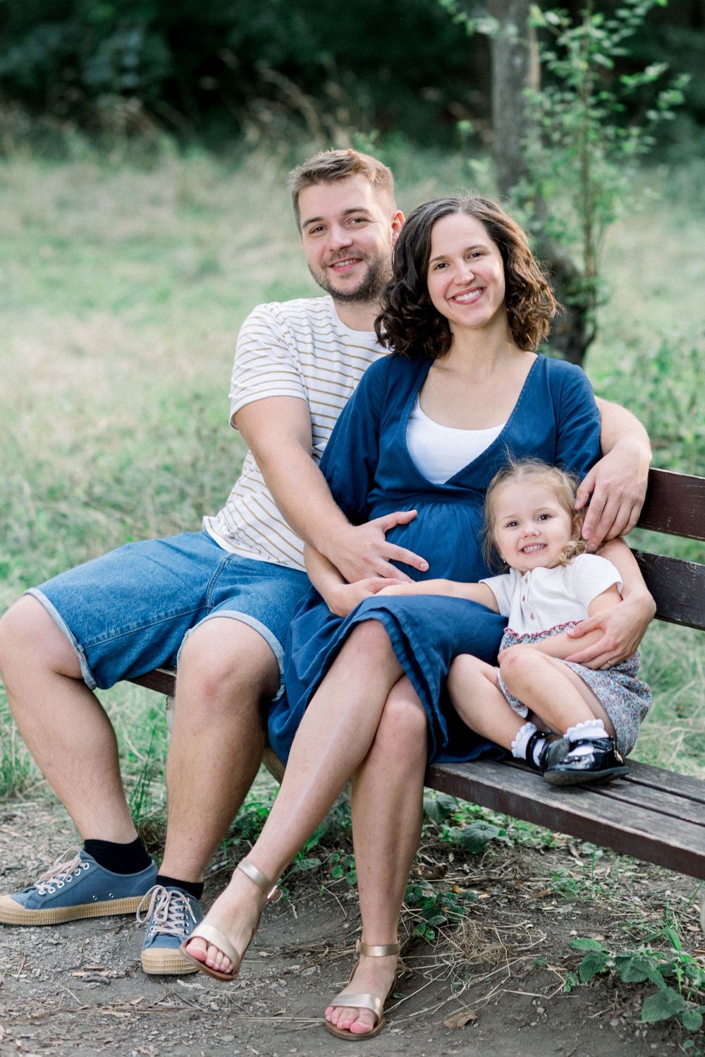 A family sits together on a wooden bench surrounded by greenery.