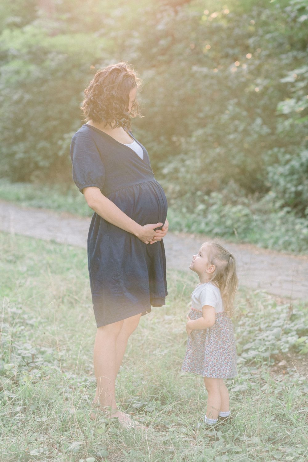 A tender moment between parent and child outdoors in a sunlit wooded area.